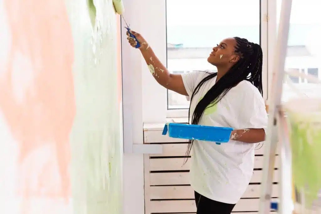Afro woman painting the walls of new home. Renovation, repair and redecoration concept