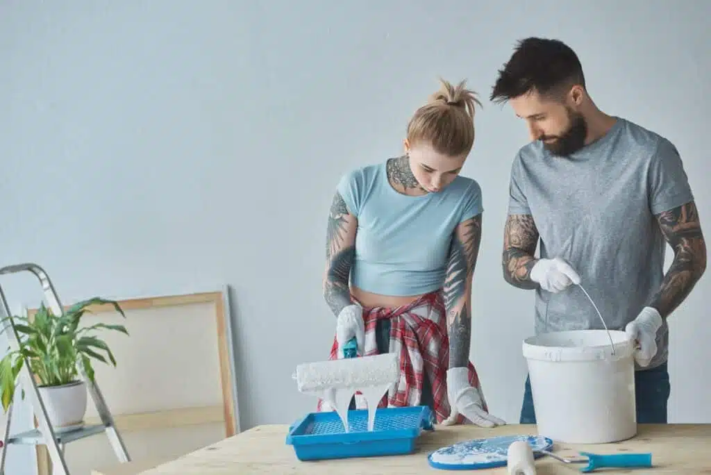 tattooed couple with roll paint brushes doing home repairment at new apartment